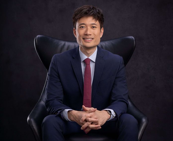 Dr. Jonathan Dang in dark blue suit and maroon tie sitting in chair
